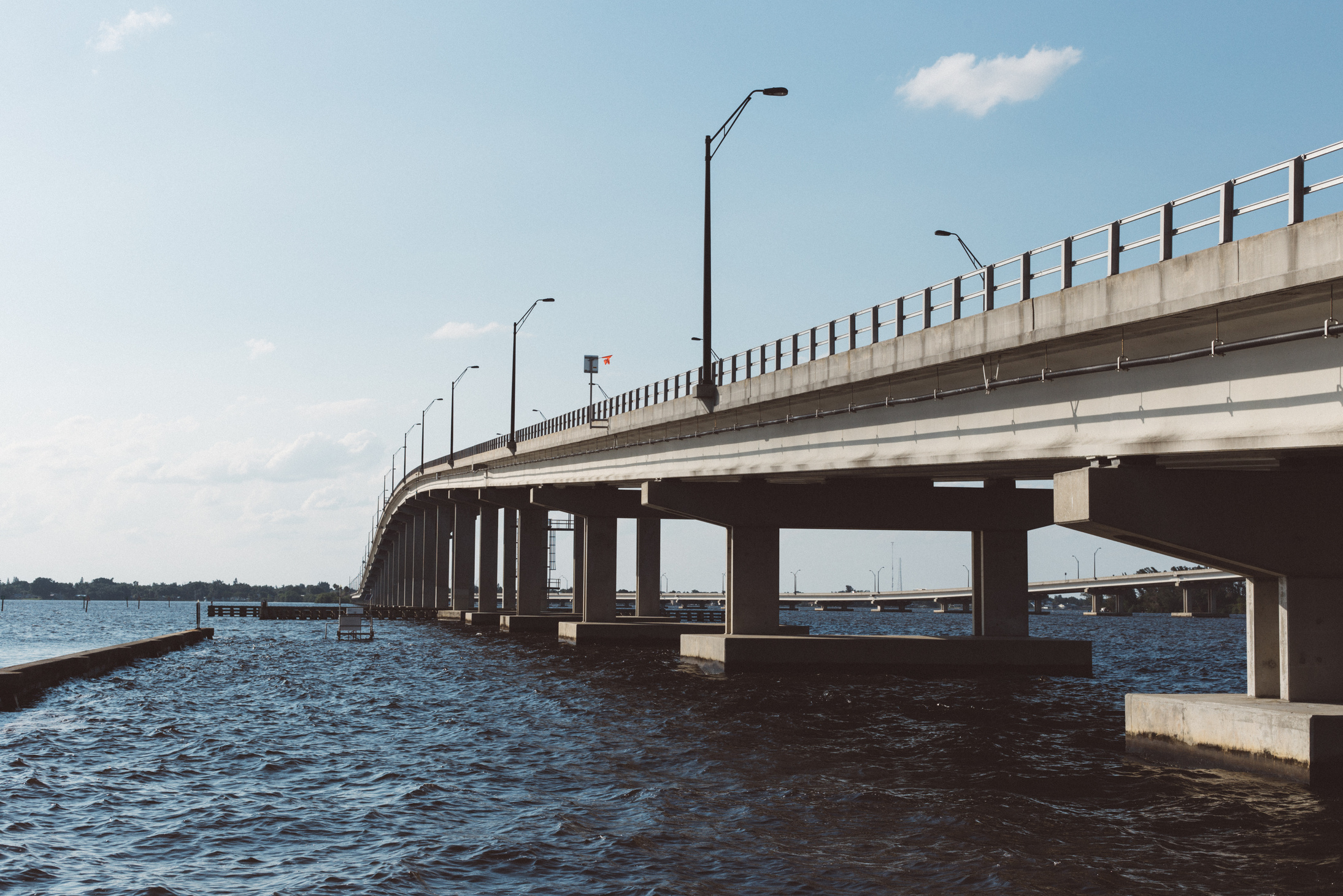 Brown Concrete Bridge Above Body of Water Under Blue Sky and White Clouds